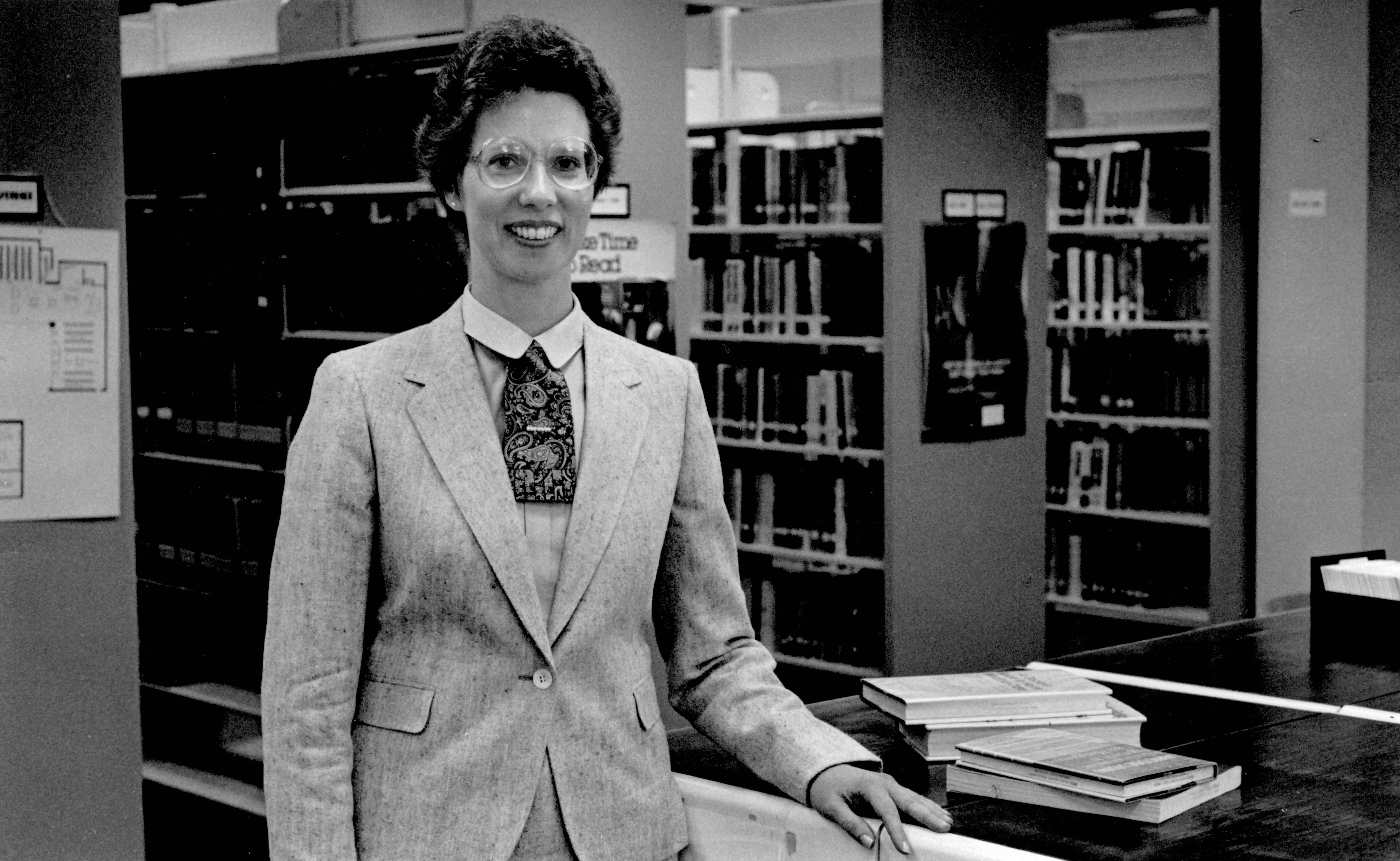 A smiling Elaine Paulette in front of the library stacks.